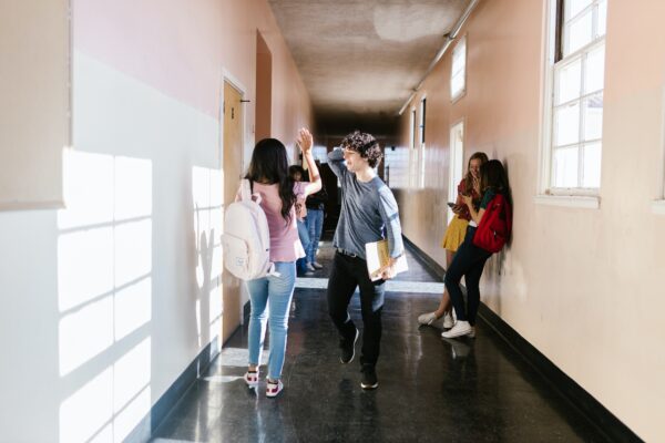 jongeren lopen door een hal op school en geven elkaar een high five