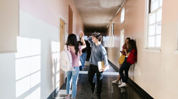 jongeren lopen door een hal op school en geven elkaar een high five