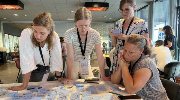 4 deelnemers aan een bijeenkomst kijken samen naar een tafel vol post-its